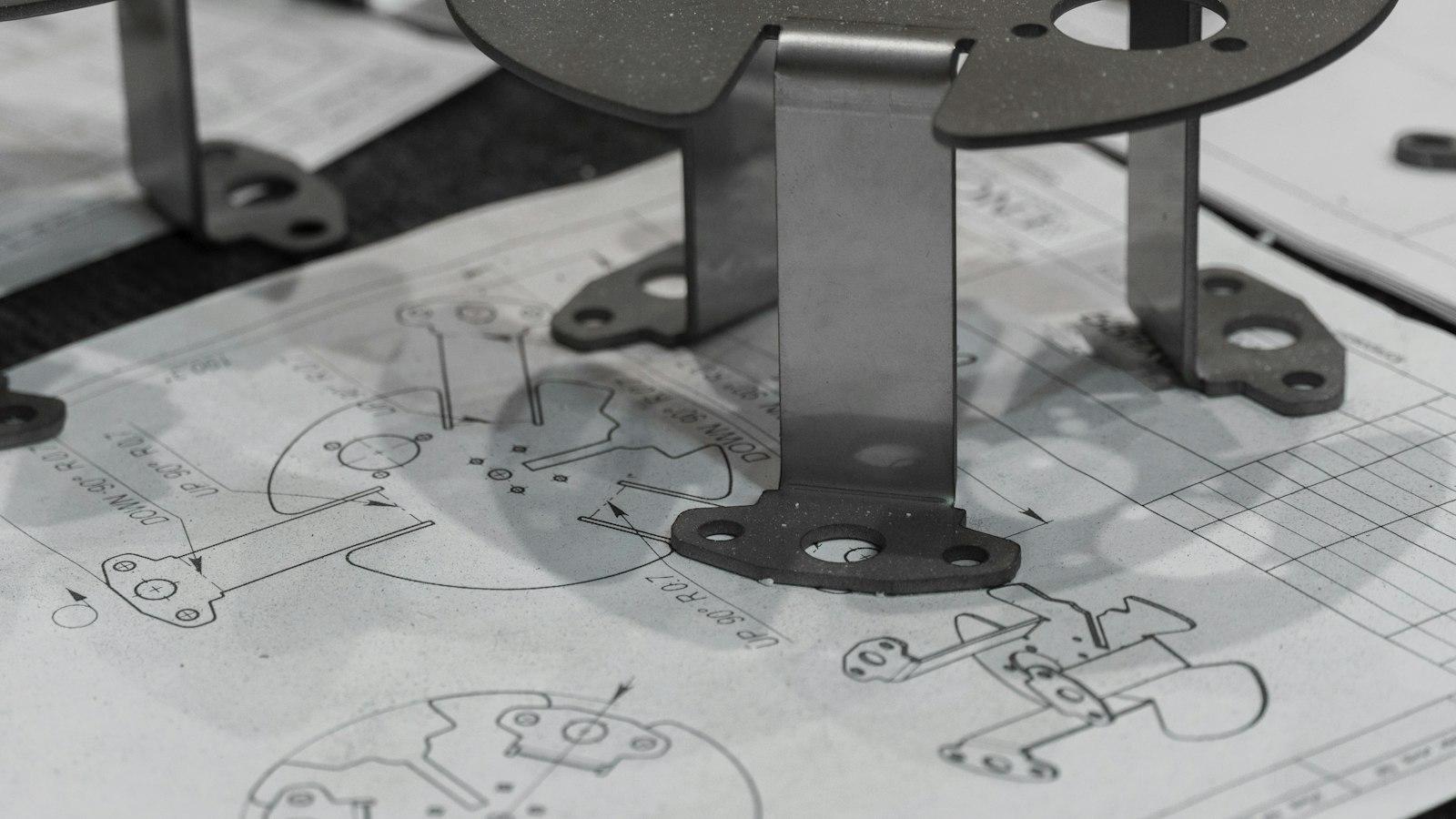 Prototype metal brackets standing on the engineering drawings they were made from